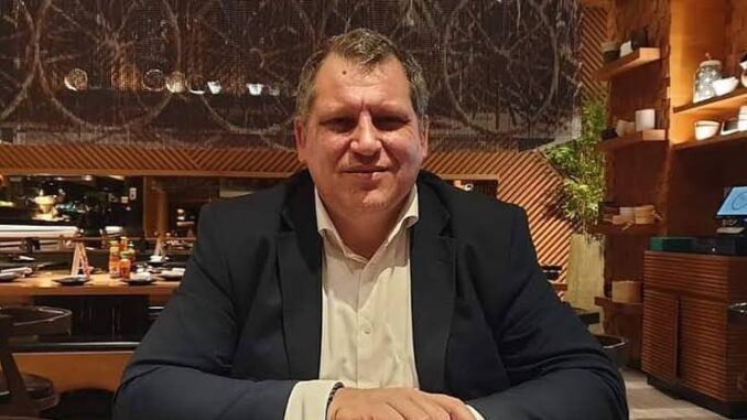 Man in a dark blazer and light shirt sitting at a table indoors. Man in a dark blazer and light shirt sitting at a table indoors.