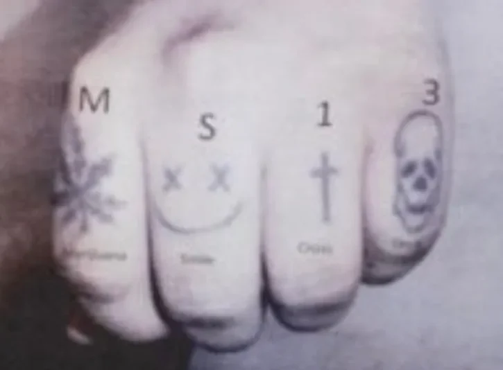 Close-up of knuckle tattoos including letters, symbols, and a skull design.