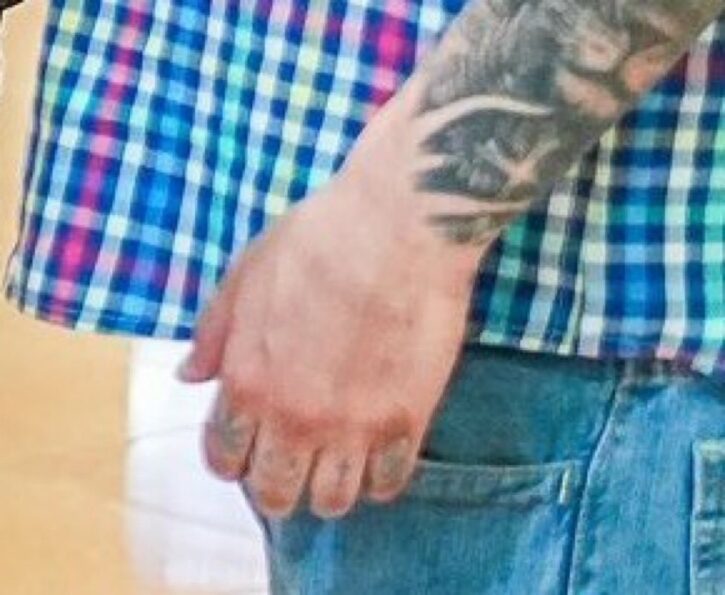 Tattooed hand resting by the side, wearing checkered shirt and jeans.