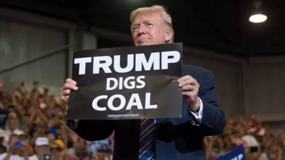 Donald Trump holding a sign that says 'Trump Digs Coal'.