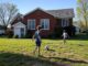 Two boys playing soccer on a sunny day in a front yard.