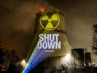 Projection of a shutdown message with a radiation symbol on a cooling tower at night.