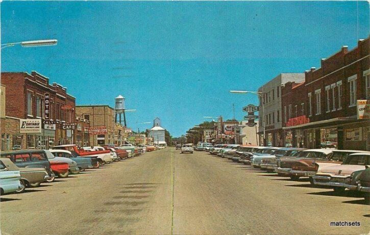 Vintage main street scene with classic cars and old buildings.