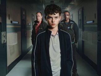 A young boy stands in a dimly lit hallway with two men behind him.