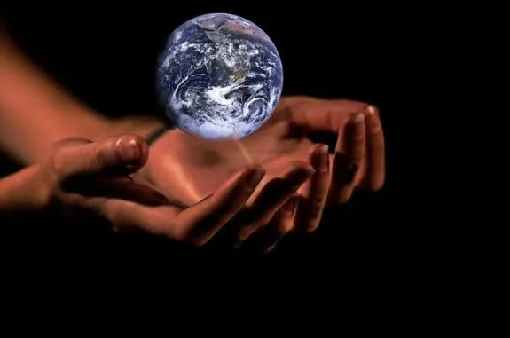 Hands gently holding a glowing Earth against a black background.