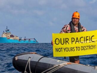 Man on a boat holding a protest sign about pacific debris.