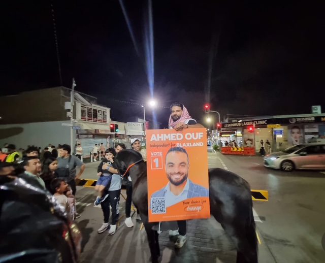 Crowd gathered at night with a large political campaign poster.