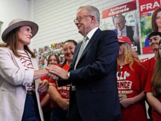 A man and a woman shake hands at a political event with supporters.
