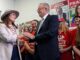 A man and a woman shake hands at a political event with supporters.