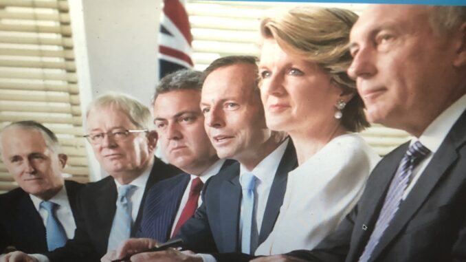 Four people in formal attire seated at a table with a British flag in the background.