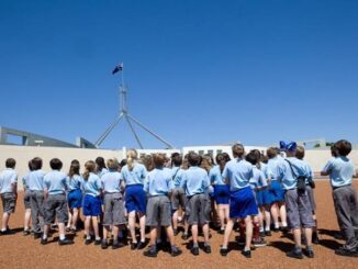 School children in uniforms gathered outside a government building under a clear blue sky.