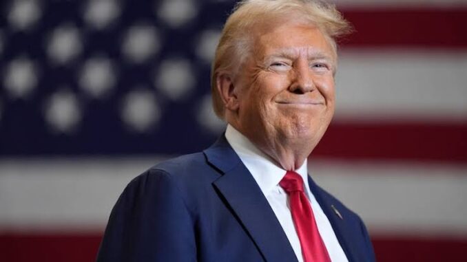 A man in a suit with an American flag backdrop.
