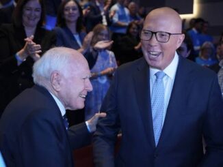 Two men in suits smiling and conversing at an event with an applauding audience.