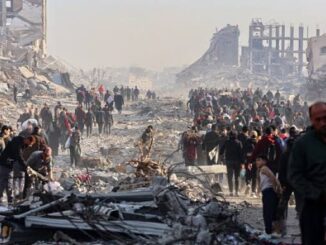 People walk through a large disaster site with rubble and debris.