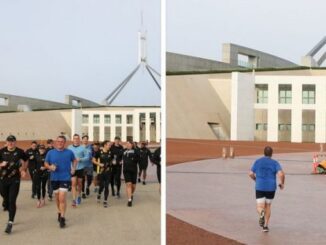 People jogging near a modern building with a wind turbine in the background.
