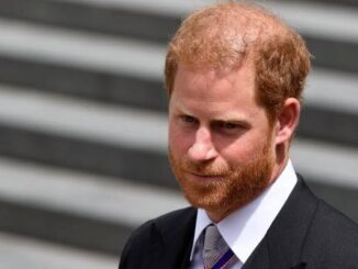 Serious man with red hair and beard in formal attire outdoors.