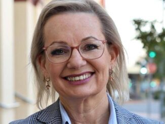 Smiling middle-aged woman wearing glasses and a checked blazer.