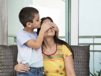 Young boy kisses his smiling mother on the forehead, covering her eyes playfully.