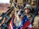 A kangaroo wearing a US flag cape with a soldier blurred in the background.