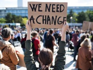 Person holding sign saying 'We Need A Change' at protest.