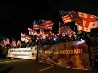 Crowd holding American and Georgian flags at night with supportive banners.