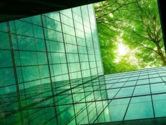 Glass building reflecting green trees under sunlight.