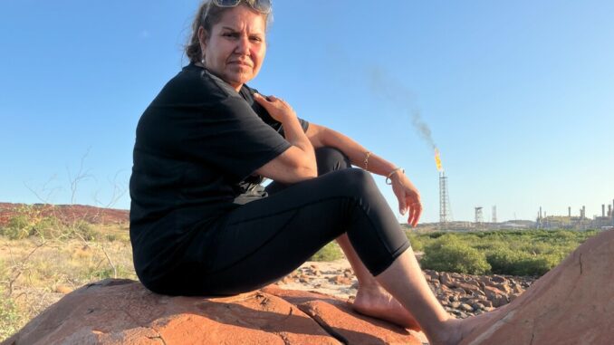 A person sitting on a rock with a smokestack in the background at sunset. A person sitting on a rock with a smokestack in the background at sunset.