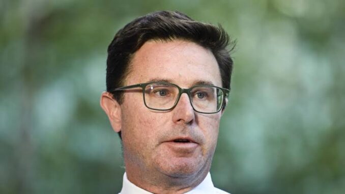 Man wearing glasses speaking outdoors with green blurred background.