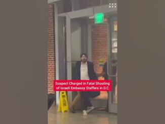 Man in a suit walking out of a building with a news caption about a suspect charged in a fatal shooting.