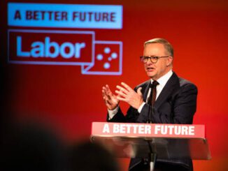 A man in a suit speaks at a podium with a Labor Party backdrop.