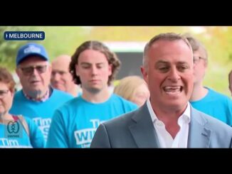 A man speaking passionately in front of a crowd wearing blue shirts.