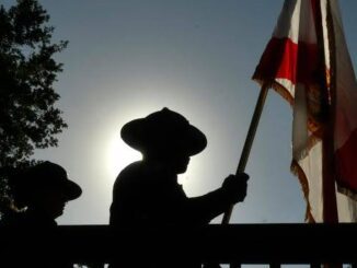 Silhouetted figure holding a flag against a glowing sunset.