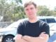 Man in black shirt with arms crossed standing outdoors.