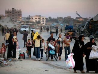 Group of people walking on a dusty road with bags and belongings.