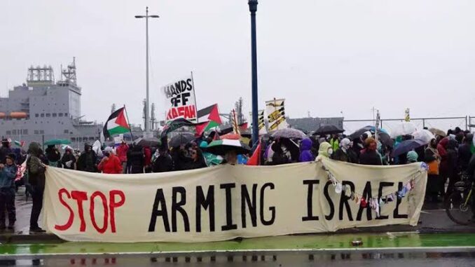 Protesters holding a banner saying 'Stop Arming Israel' with Palestinian flags. Protesters holding a banner saying 'Stop Arming Israel' with Palestinian flags.