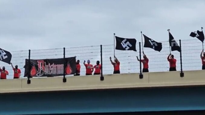 People on a bridge hold black flags and a banner under a cloudy sky. People on a bridge hold black flags and a banner under a cloudy sky.