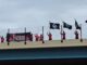 People on a bridge hold black flags and a banner under a cloudy sky.