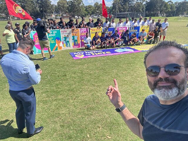 Group photo of people holding colorful banners outdoors on a sunny day.