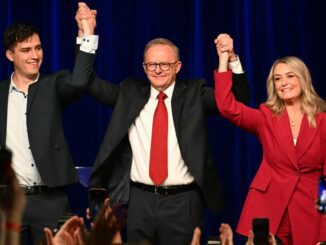 Three people on stage holding hands, celebrating.