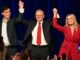 Three people on stage holding hands, celebrating.