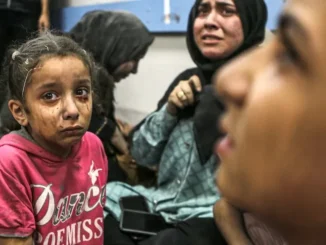 A young girl looks worried while adults in the background appear distressed.