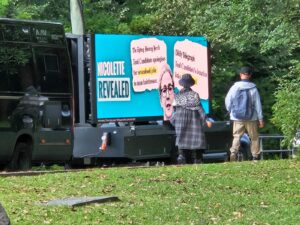 People gather around a van with a sign saying 'Molecule Revealed' in a park.
