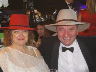 A smiling couple dressed elegantly with hats at a formal event.