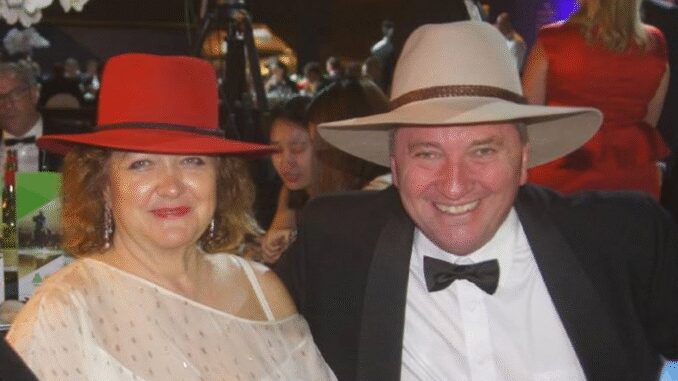 A smiling couple dressed elegantly with hats at a formal event.