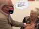 Two older adults exchanging a lighthearted moment, one wearing a mask with a flag design.