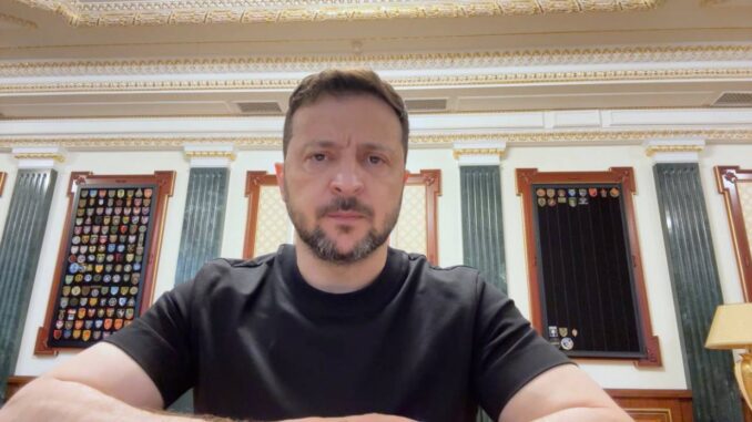 A man in a black shirt sitting indoors with ornate decor behind him.