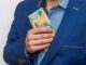 Person in blue suit pocketing cash discreetly.