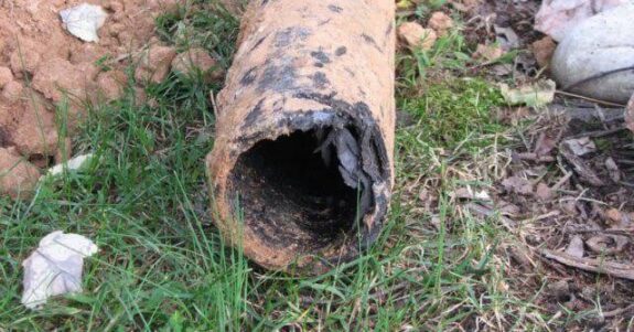 Rusty, broken pipe lying on grass outdoors.