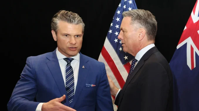 Two men in suits shaking hands in front of American flags.