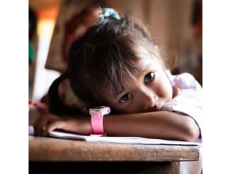 A young girl resting her head on a table, looking thoughtful.